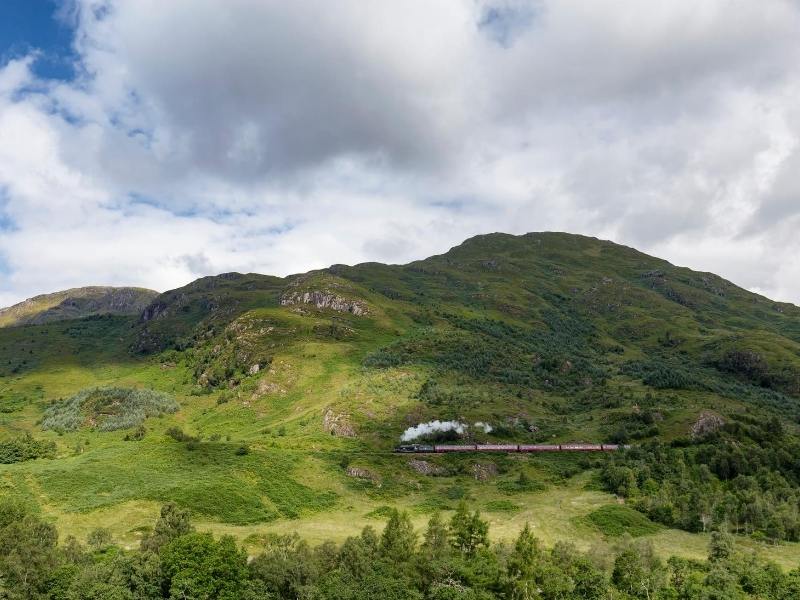 Steam train crossing green countryside in Scotland