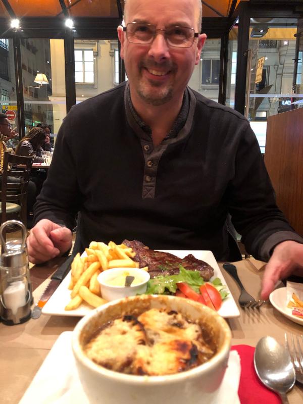 Paris restaurant with a man eating a plate of steak and chips and a bowl of French onion soup.