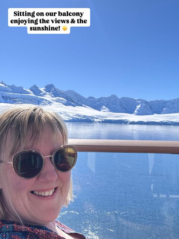 Tracy Collins in sunglasses taking a selfie from a ship balcony, with snowy mountains and blue water behind and a text caption about enjoying the views
