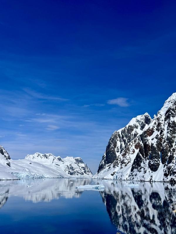 Dramatic dark mountains and a floating iceberg under blue sky on an Antarctica expedition cruise