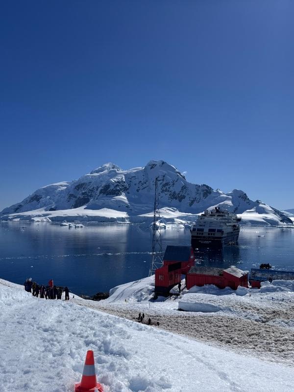 Expedition passengers coming ashore by zodiac below a red research station in Antarctica