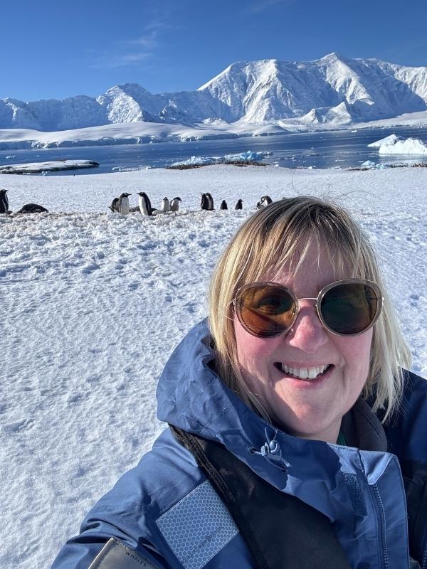 Penguins gathered on snow beneath towering Antarctic mountains