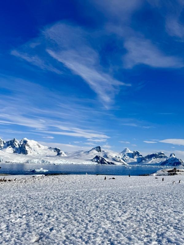 Tiny figures crossing a vast snow-covered plain beneath Antarctic mountains