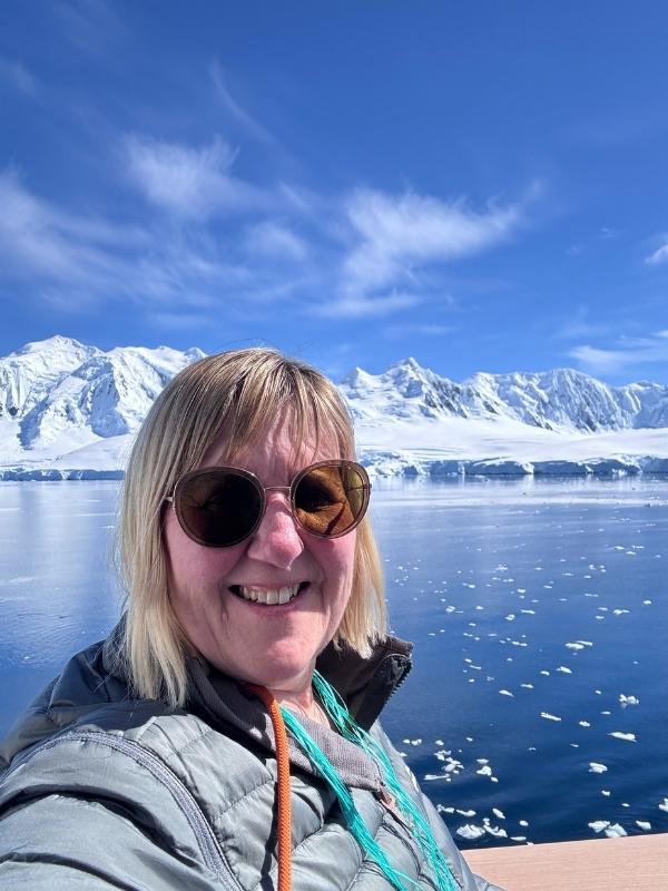 Tracy in sunglasses enjoying bright sunshine with icebergs behind on an Antarctica cruise
