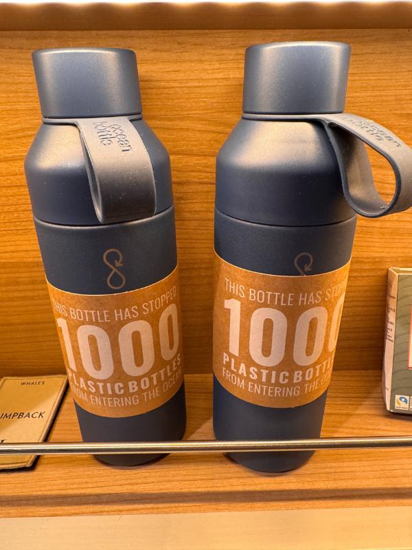 Two reusable Ocean Bottles on a wooden shelf in the onboard shop, each labelled as having stopped 1000 plastic bottles entering the ocean