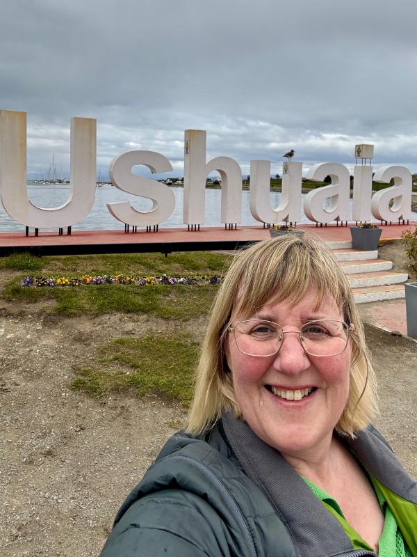 Tracy smiling in front of the large white Ushuaia letters beside the harbour