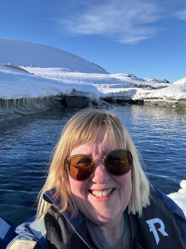 Tracy in an expedition jacket beside calm water and snowy mountains in Antarctica